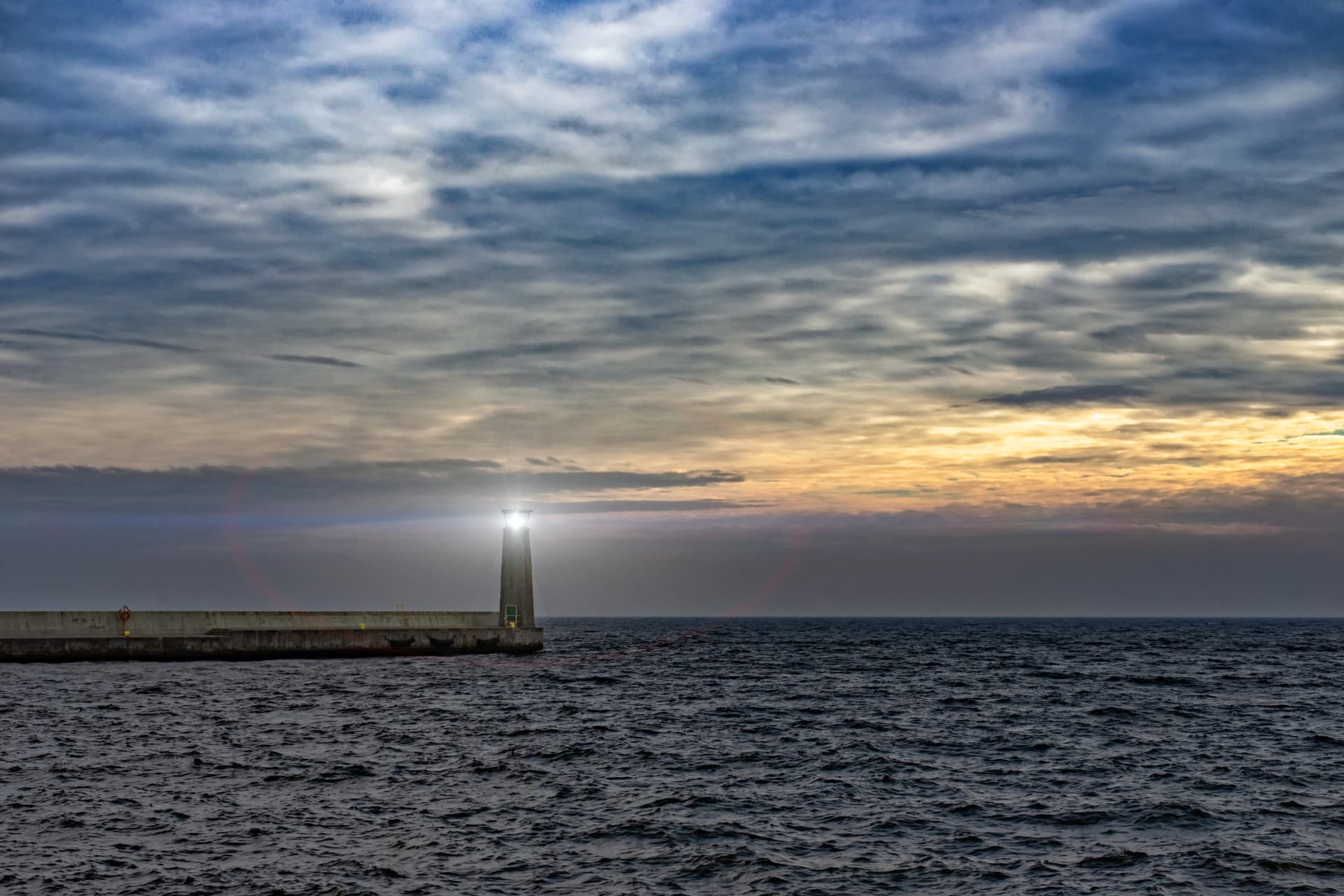 Farol aceso junto ao mar ao entardecer, oferecendo referência no horizonte.